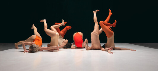Legs up. Group of young girls, experimantal dancers performing on stage in bodysuits. Creative and...