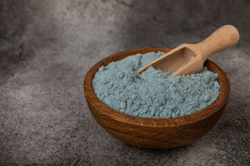 Blue spirulina powder in a bowl on a black marble background. Natural superfood, vegan, healthy food supplement. Phycocyanin extract. Antioxidant. Place for text. Copy space.