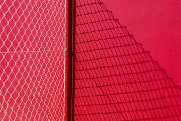 Red painted wall with a wire fence, abstract with shadow.