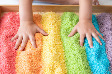 Hands in a rainbow sensory bin