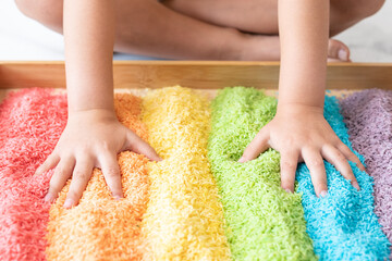 Hands in a rainbow sensory bin