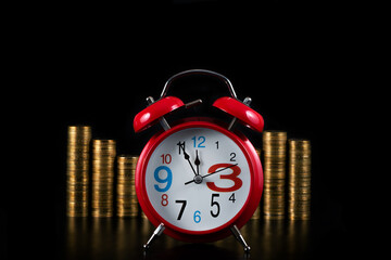 Red classic alarm clock on the background of stacked gold coins