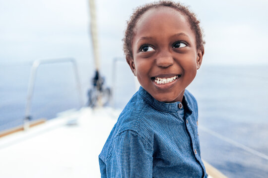Cheerful black boy smiling and looking away on yacht