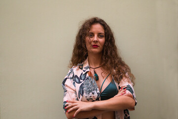 young blonde woman with curly hair and blue eyes crossing her arms and making different gestures and expressions in front of a beige wall. Concept expressions.