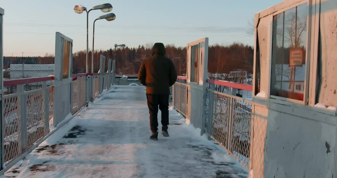 A man walks along an elevated railroad pedestrian crossing in winter.