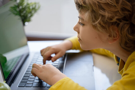 Close-up of child hands typing on the keyboard laptop. Distance learning online education. Schoolboy girl studying at home with digital tablet notebook and doing school homework. Side view