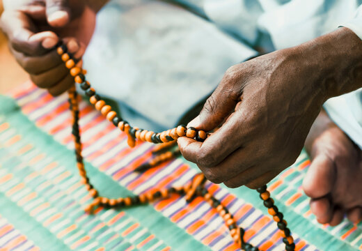 Muslim man sitting on a colorful mat and praying while he is handling a rosary, photo