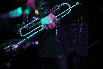 A woman in a black shiny dress holds a musical instrument trumpet in her lowered hand