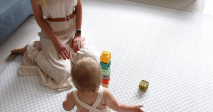 Young caucasian mother or nanny playing with cute baby one year old, learning development toy for infant kids. Two generation family spending time together and enjoying life on floor at home