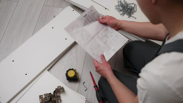 The furniture assembler is studying the instructions for assembling furniture, there are boards, screws nearby. Self-assembly of furniture. The concept of moving, repair. Close-up