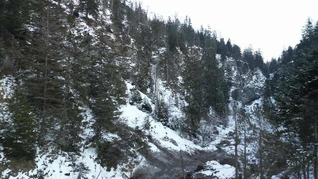 the stuiben falls in the mountains near the town of reutte in austria with trees and mountains covered with snow. the waterfall is slightly frozen taken with a drone