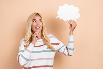 Photo of mature aged intelligent woman blonde wavy hair touch chin minded look interested hold paper cloud idea isolated on beige color background
