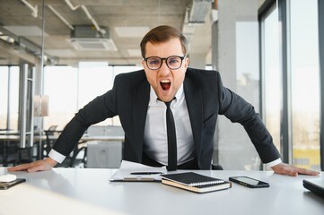 Angry businessman sitting at his desk and screaming at his employees.