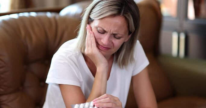 Woman holding pain pills and suffering from toothache at home