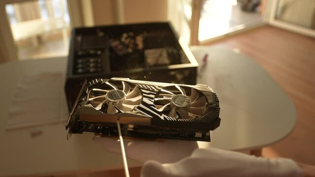Extreme close-up of unrecognizable professional computer master in gloves cleaning video graphic card using with compressed air spray, slow motion. Concept of desktop PC maintenance and service.