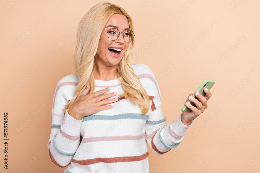 Sticker Photo of cheerful cute woman with curly hairstyle striped long sleeve hand on chest look at phone isolated on pastel color background