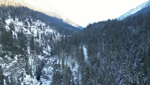 the stuiben falls in the mountains near the town of reutte in austria with trees and mountains covered with snow. the waterfall is slightly frozen taken with a drone