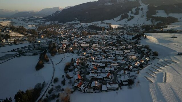 the small idyllic town of nesselwang in the south of bavaria in germany filmed with a drone in winter with snow covered hills and mountains in the background also covered with snow