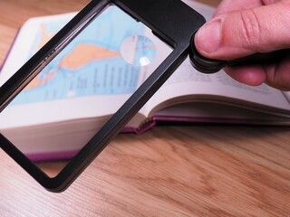 Hand holding magnifying glass. Open book with magnifying glass on wooden desk. Vision problems and...