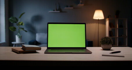 Close up shot of modern chroma key green screen laptop computer set up for work on desk at night -...