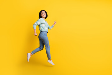 Fototapeta na wymiar Full length photo of good mood satisfied girl dressed blue cardigan jeans running clenching fists isolated on yellow color background