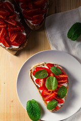 Top vertical close up view of bruschetta on a plate with cherry tomatoes, cream cheese and mint leaves on a wooden table
