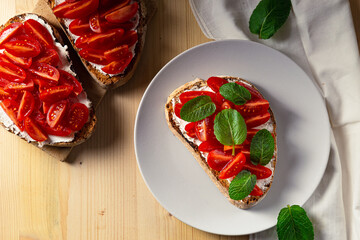 Top close up view of bruschetta on a plate with cherry tomatoes, cream cheese and mint leaves on a...