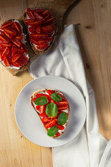 Top vertical view of bruschetta on a plate with cherry tomatoes, cream cheese and mint leaves on a wooden table