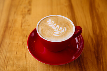 Aromatic coffee in a red cup with milk foam and latte art on table.