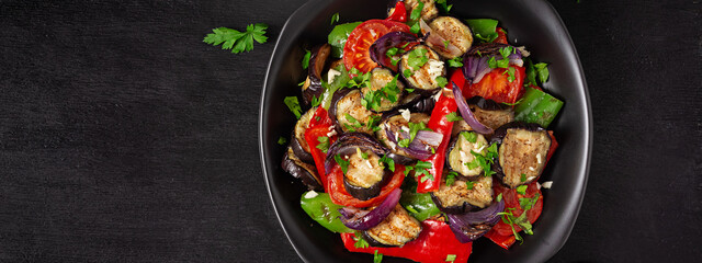 Grilled vegetables eggplant, bell pepper, zucchini, red onion, tomato with garlic on a black plate. Top view, banner