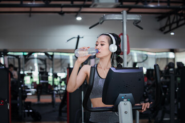 Fototapeta na wymiar Fitness woman with headphones drinking water while resting on treadmill in gym. Healthy lifestyle concept.