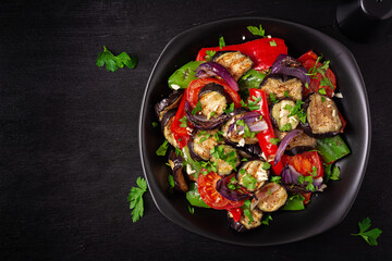 Grilled vegetables eggplant, bell pepper, zucchini, red onion, tomato with garlic on a black plate. Top view, above