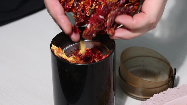 A man pours dried red peppers into a coffee grinder. Grinding hot pepper. Close-up.