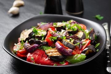 Grilled vegetables eggplant, bell pepper, zucchini, red onion, tomato with garlic on a black plate.