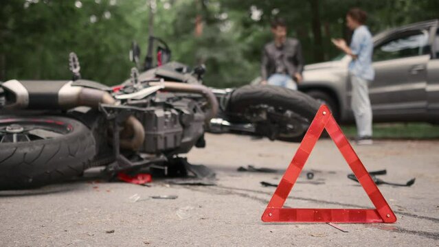 Damaged motorbike and car on the city road at the scene of an accident. Red emergency stop triangle sign on road in car accident scene.
