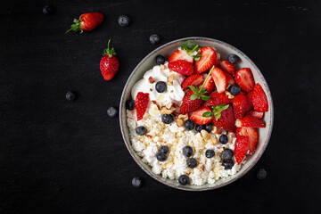 Cottage cheese, curd cheese with fresh strawberries, blueberries, nuts and yogurt in a bowl.  Healthy dairy product rich in calcium and protein. Top view, above