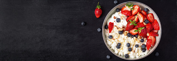 Cottage cheese, curd cheese with fresh strawberries, blueberries, nuts and yogurt in a bowl.  Healthy dairy product rich in calcium and protein. Top view, banner © timolina