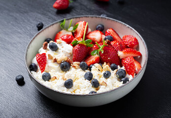 Cottage cheese, curd cheese with fresh strawberries, blueberries, nuts and yogurt in a bowl.  Healthy dairy product rich in calcium and protein.