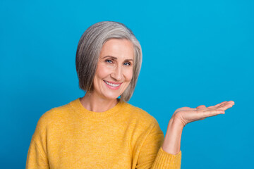 Photo portrait of senior gorgeous woman palm hold empty space product dressed stylish yellow garment isolated on blue color background