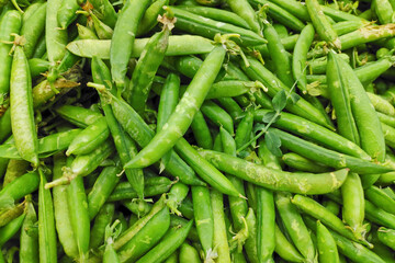 Stack of green peas in their pods on a market stall