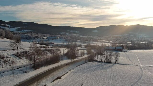 Drone film stock in winter Norway - flying over road in rural winter landscape - with surrounding farms