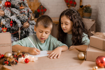 boy and girl write a letter with Christmas wishes to Santa Claus, sitting at a wooden kitchen table