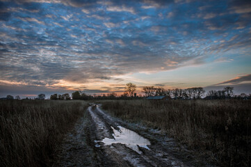 The field road between the villages is covered with puddles that reflect the colors of the dawn sun.