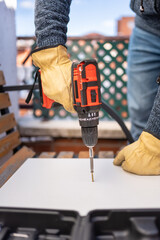 Men's hands holding a screw to screw it with a battery-powered electric machine into a wood.