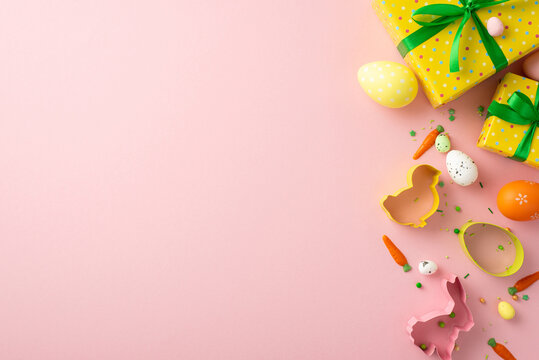 Easter concept. Top view photo of yellow gift boxes with green bows colorful easter eggs baking molds and carrot shaped sprinkles on isolated pastel pink background with blank space