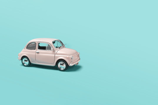 Miniature pale pink toy car on green background with copyspace