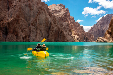 Kayaking on a mountain lake. Two men are sailing on a red canoe along the lake along the rocks. The...