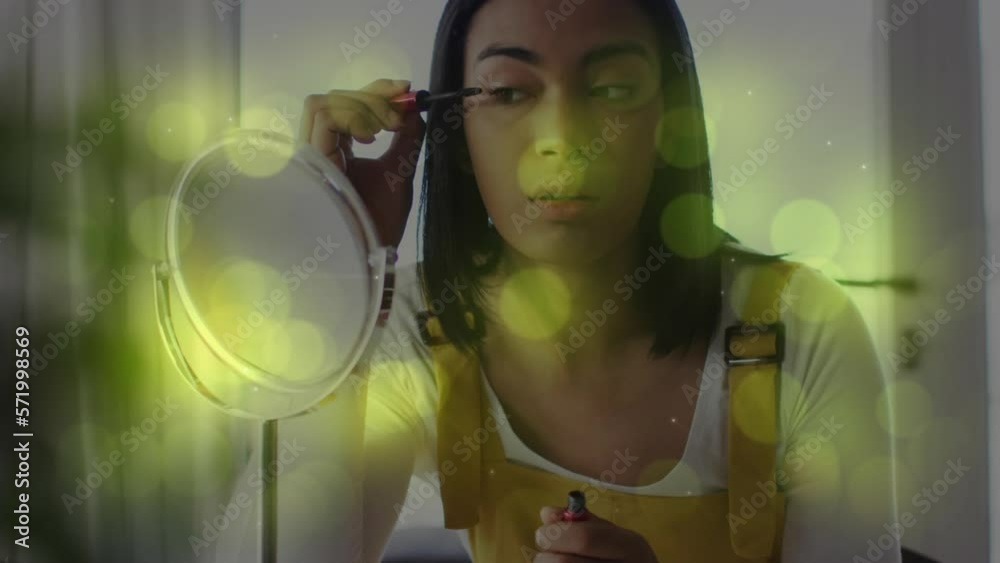 Canvas Prints Animation of light spots over biracial woman applying mascara