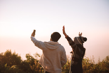 Two people traveller using smartphone selfie together with nature view at sunrise time. Travel and recreation concept on vacations.