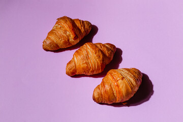 Three delicious fresh croissants on a purple background. Creative minimalistic design for baking and coffee shop advertising